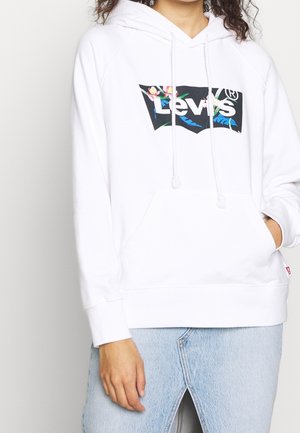 Person trägt weißen Levi's Hoodie mit floralem Logoaufdruck und hellblauen Jeansrock mit Frontschlitz, Hand in der Tasche.