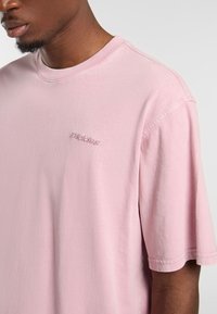 Ljust rosa bomullströja med rund halsringning. Har korta ärmar och diskret broderi med texten "Daddies!" på bröstet. Mjuk textur.