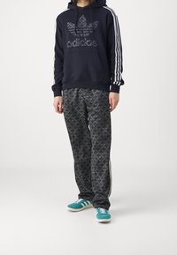 Navy blue hooded sweatshirt with white Adidas branding, paired with black patterned sweatpants featuring a repeating logo design and white stripes.