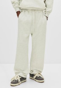 Person wearing light gray wide-leg sweatpants with hands in pockets and gray black sneakers with thick cream laces.