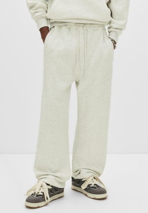 Person wearing light gray wide-leg sweatpants with hands in pockets and gray black sneakers with thick cream laces.