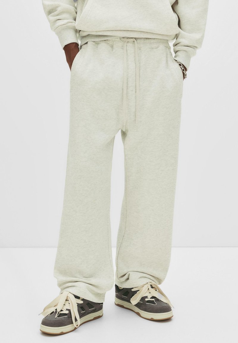 Person wearing light gray wide-leg sweatpants with hands in pockets and gray black sneakers with thick cream laces.