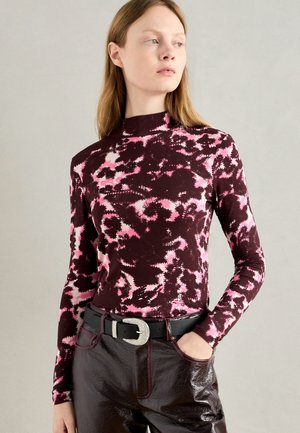 Long-sleeve top in dark burgundy with a pink abstract pattern. High neckline and fitted design paired with shiny brown trousers, accented by a belt.