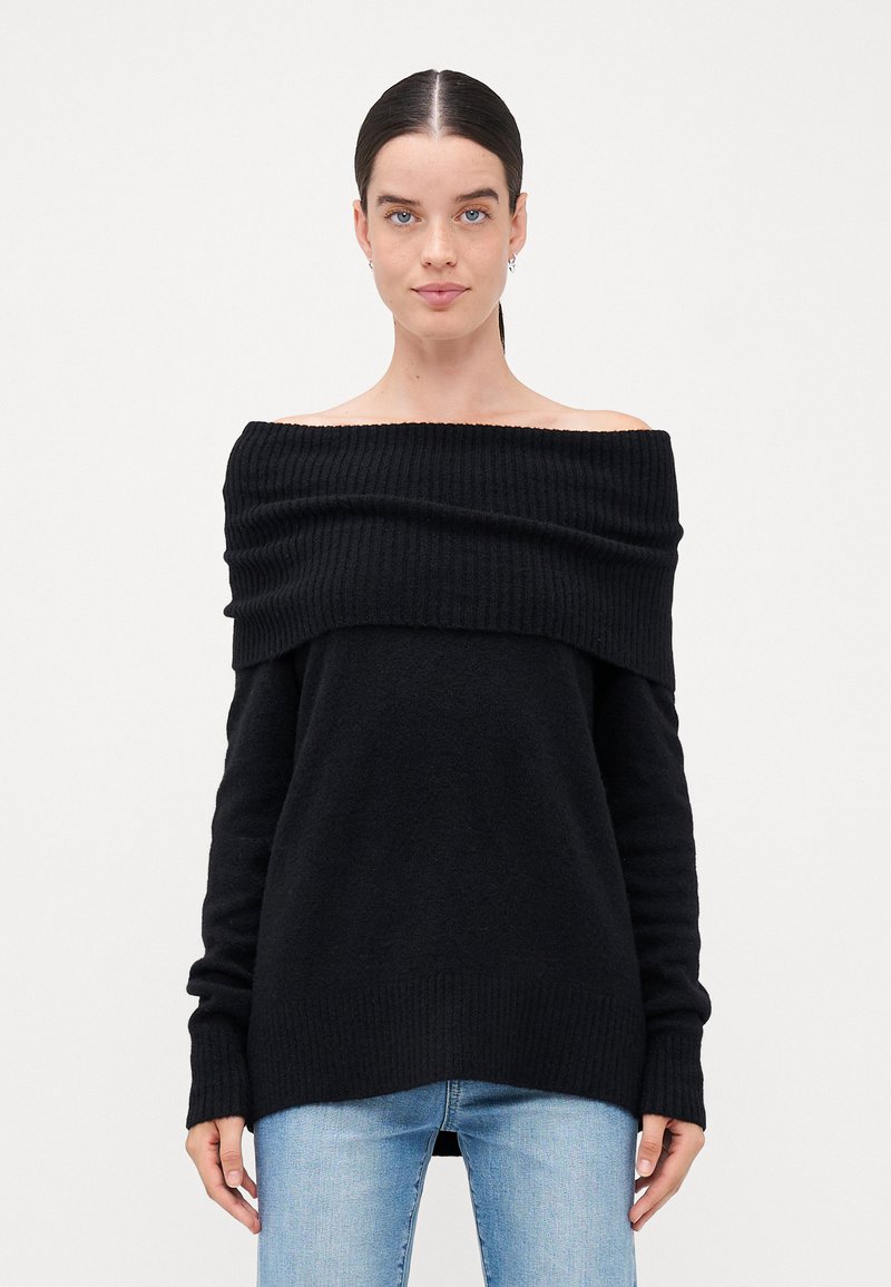 Schwarzer Off-Shoulder-Pullover mit gerippter Textur, langen Ärmeln und lockerer Passform, kombiniert mit hellblauen Jeans.