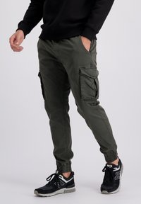 Pantalones cargo de algodón en verde oliva, con puños elásticos, múltiples bolsillos laterales y un ajuste relajado; combinados con zapatillas deportivas negras.