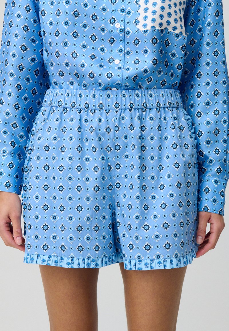Pantalones cortos azules con un patrón, confeccionados en una tela suave, con una cintura elástica, dobladillo con volantes y diseños geométricos en azul oscuro y blanco.