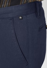 Marineblaue Hosen aus strukturiertem Stoff, mit einer sichtbaren Tasche, einer genähten Detail und einem markierten Etikett in der Nähe des Bundes.