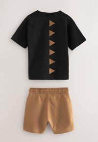 Chemise noire à manches courtes avec cinq pointes triangulaires marron dans le dos, associée à un short marron à taille élastique.