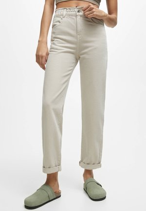 Jean beige taille haute avec une coupe décontractée, ornés de revers et d'une taille élastique. Associés à des sabots verts à enfiler.