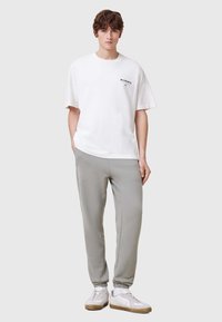 Vit bomull t-shirt med svart logotyp på bröstet, parat med ljusgrå sweatpants. Skorna är vita med grå detaljer och texturerad sula.