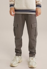 Ruskot ja tummansiniset ruutukuosiset cargo-housut, joissa on kaksi sivutaskua, elastiset hihnat ja rento mitoitus, yhdistettynä valkoisiin urheilukenkihin.