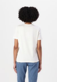 Hvid bomulds t-shirt med korte ærmer, rund halsudskæring og en afslappet pasform. Båret med lyseblå jeans, vist fra bagsiden.