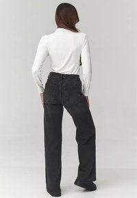 Czarne dżinsy z wysokim stanem i prostymi nogawkami, z dwoma tylnymi kieszeniami i subtelnymi detalami przeszycia. W zestawieniu z białą koszulą z długim rękawem.