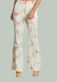 Hoge taille, wijde crème broek met een zachte roze en groene bloemenprint, gedragen met beige puntige hakken.