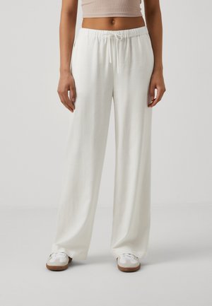 White, lightweight, loose-fitting pants with an elastic waistband and drawstring. Smooth texture, wide leg design, paired with white sneakers.