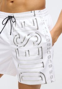 Witte zwembroek met een zwarte tekstpatroon met de frase "FOR SUCCESSFUL LIVING." Elastische tailleband met trekkoord detail.