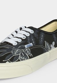 Μαύρο αθλητικό παπούτσι Vans με λευκά κορδόνια και γκρι λουλουδάτο σχέδιο στο καμβά επάνω μέρος, με λευκή λαστιχένια σόλα και ετικέτα με το λογότυπο Vans.