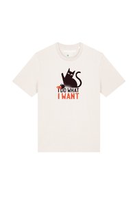 Licht beige t-shirt met een zwarte kattengrafiek en rode tekst met de opschrift "IK DOE WAT IK WIL." Korte mouwen en ronde halslijn.