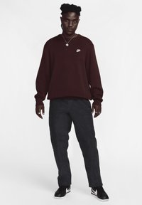 Mørk burgunder sweatshirt med et lille hvidt Nike-logo, parret med mørkegrå bukser og sorte sneakers med hvide detaljer. Casual fit.
