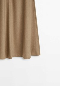 Jupe en laine marron en forme trapèze avec un tombé souple et un détail de couture visible, suspendue sur un fond blanc.