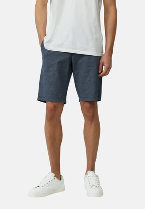 Shorts bleu marine avec un motif à carreaux subtil, fabriqués en tissu léger, dotés de poches latérales et d'une coupe droite. Associés à des baskets blanches.