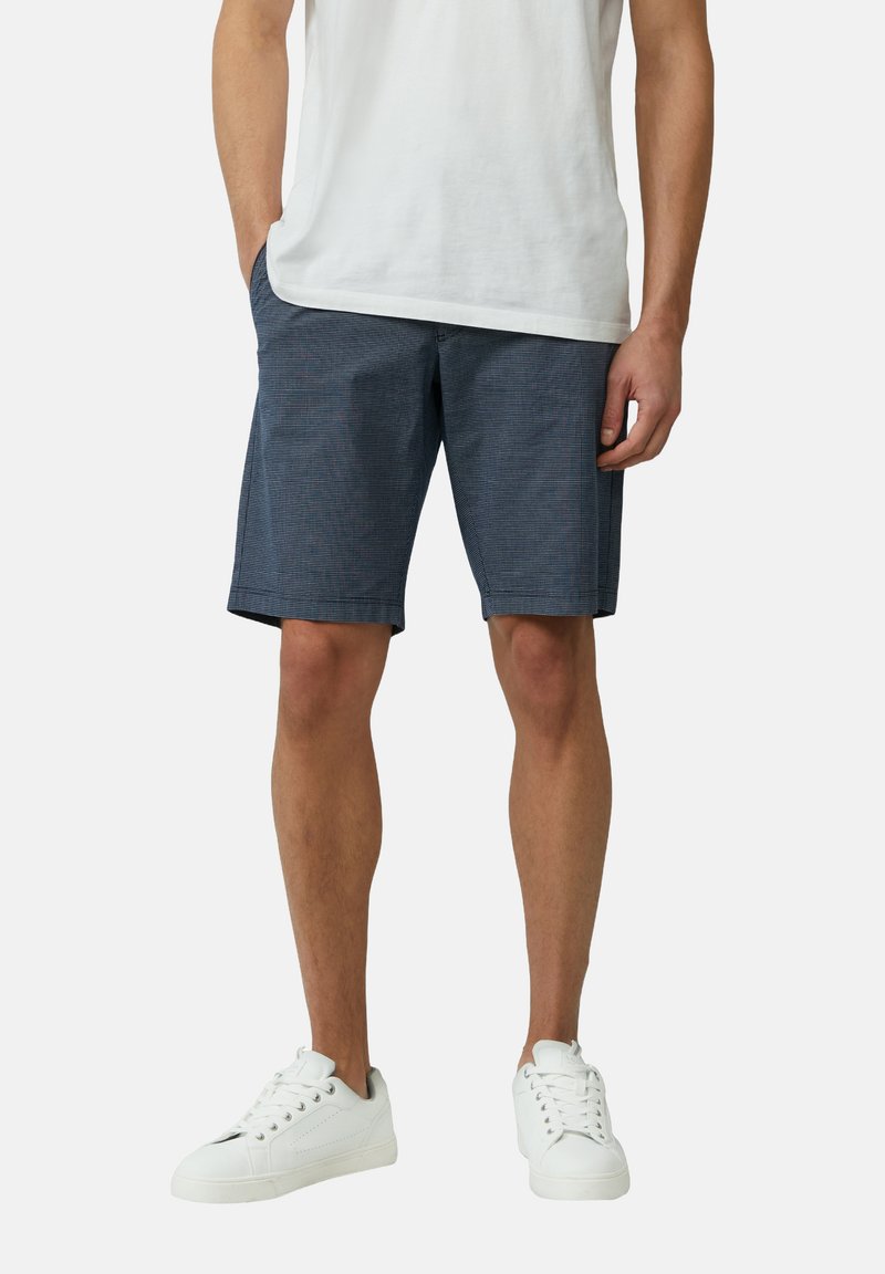 Marineblaue Shorts mit einem dezenten Karomuster, aus leichtem Stoff gefertigt, mit Seitentaschen und geradem Schnitt. Kombiniert mit weißen Sneakers.