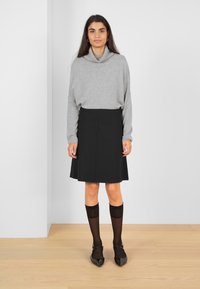 Pull à col cheminée gris associé à une jupe noire évasée. Chaussettes en dentelle noires montantes et ballerines noires à bout pointu. Tissu lisse, design minimal.