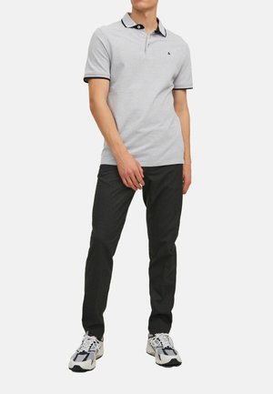Grijze polo met zwarte kraag en mouwaccenten, twee knopen, gedragen met donkere broek en veelkleurige sneakers. Eenvoudig, casual ontwerp.