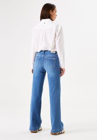 Hoge taille blauwe denim flare broeken met twee achterzakken, onafgewerkte zoom en een gestructureerde afwerking, gecombineerd met een wit overhemd met knopen.