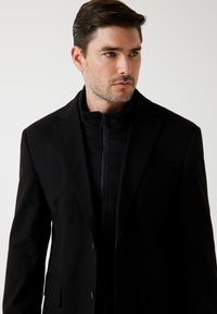 Zwarte buitenjack met een op maat gemaakt ontwerp, met een met rits sluitende binnenlaag met horizontale padding. Soepele textuur en gestructureerde vorm.