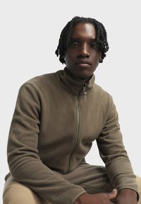 Fleece-Trainingsjacke in Olivgrün, mit hohem Kragen und durchgehend weichem Textil. Reißverschluss und eng anliegende Bündchen.