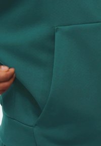 Tyrkysová látka s hladkou textúrou, obsahujúca bočné vrecko. Látka sa zdá byť elastická a jemná, vhodná na neformálne nosenie.