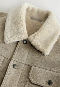 Tan uldjakke med en cremefarvet faux-fur krave. Har metal trykknapper og lommer med klap. Blød tekstur med et rent, struktureret design.