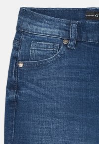 Jeans en denim bleu foncé avec une texture lisse, dotés d'une poche avant, d'accents en métal et d'une ceinture classique.