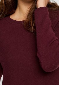 Bordeauxfarbener Strickpullover mit Rundhalsausschnitt und langen Ärmeln, der über eine gerippte Textur und eng anliegende Bündchen verfügt.