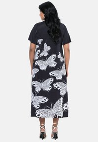 Maxikleid aus schwarzem Stoff mit weißem Schmetterlingsdruck, kurzen Ärmeln und lockerem Schnitt. Abgerundet mit High-Heel-Sandalen.