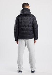 Black puffer jacket with horizontal stitching and a hood, paired with light gray sweatpants and navy accented sneakers. Minimalistic design.