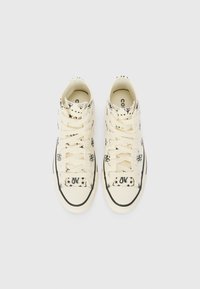 Hochschaft-Sneaker aus cremefarbenem Canvas mit schwarzen grafischen Mustern, ausgestattet mit einem Schnürdesign, gummiertem Zehenbereich und kontrastierender schwarzer Sohle.