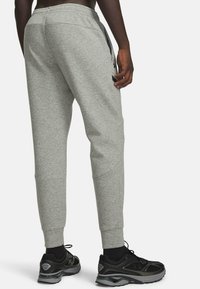 Graue Jogginghosen aus weichem Stoff mit elastischem Bund und zulaufenden Beinabschlüssen. Verfügen über seitliche Taschen und einen Logo-Akzent am Oberschenkel.