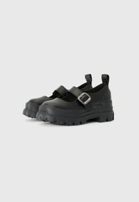 Scarpe nere con cinturino a fibbia e suola in gomma spessa, realizzate in materiale sintetico morbido e dotate di linguette posteriori per una facile calzata.