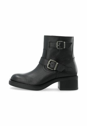 Bottine en cuir noir avec deux boucles en métal, bout arrondi, talon bloc robuste et finition texturée. Détail de couture latérale visible.