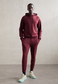 Burgundowa bluza z kapturem z sznurkiem i rękawami raglanowymi, zestawiona z dopasowanymi spodniami dresowymi. Uzupełniona beżowymi trampkami z turkusowymi podeszwami.