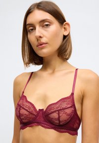 Bralette en dentelle d'un bordeaux profond avec des bretelles en satin ajustables, présentant des bords festonnés et un design en maille transparente. Idéal pour superposer.