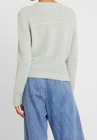 Pull vert clair texturé avec un col rond et des manches longues, associé à un pantalon en denim bleu ample.