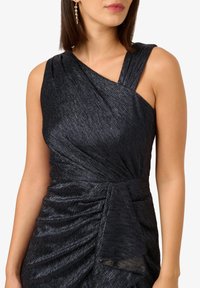 Černé šaty bez rukávů s drapovaným designem, texturovanou látkou, asymetrickým výstřihem a detaily na bočním uzlu.