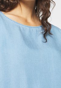 Ljusblå bomullströja med rundad krage, med subtila texturer och sömmar längs halsringningen.