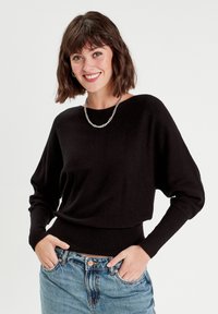 Pull noir en tricot avec une coupe décontractée, des poignets côtelés et une ceinture côtelée. Assorti à un jean en denim bleu clair, avec une fermeture à boutons classique.