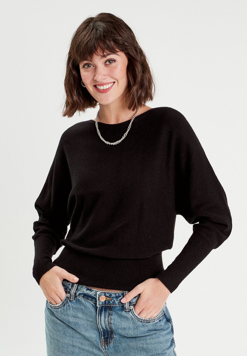 Pull noir en tricot avec une coupe décontractée, des poignets côtelés et une ceinture côtelée. Assorti à un jean en denim bleu clair, avec une fermeture à boutons classique.