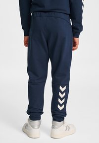 Marinblå mjukisbyxor med vitt chevronmönster på underbenen, resår i midjan och mudd vid anklarna. Mjukt tyg med en slät yta.