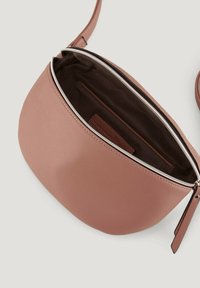 Kulatá crossbody taška světle růžové barvy z kůže s bílým zipem a tmavě hnědým podšívkou; obsahuje malou vnitřní kapsu.